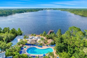 Ein Resort mit Swimmingpool, umgeben von Palmen und Liegestühlen, mit Blick auf ein großes Gewässer.