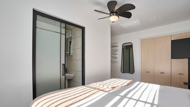 A modern bedroom with a bed, a ceiling fan, a large mirror, and a wardrobe. - Host & Stay | Hazelnut House (Launceston)