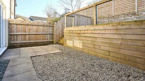 A backyard with a wooden fence, a gravel area, and a concrete pathway. - Host & Stay | Hazelnut House (Launceston)