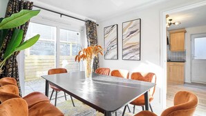 A dining area with a dark table, orange chairs, and a vase with dried flowers. There are three framed artworks on the wall. - Host & Stay | Hazelnut House (Launceston)