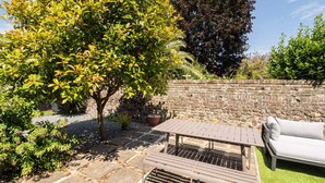 A patio area with a stone table and a white sofa, surrounded by greenery and a stone wall. - Host & Stay | Prince Albert (Margate)