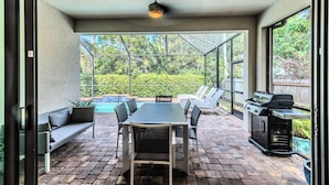 Une terrasse extérieure avec une table à manger, des chaises, un barbecue et une vue sur une piscine et un espace verdoyant.