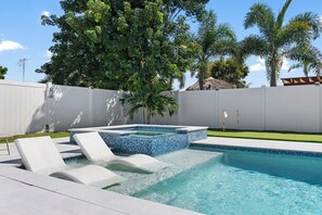 A swimming pool with a hot tub and lounge chairs.