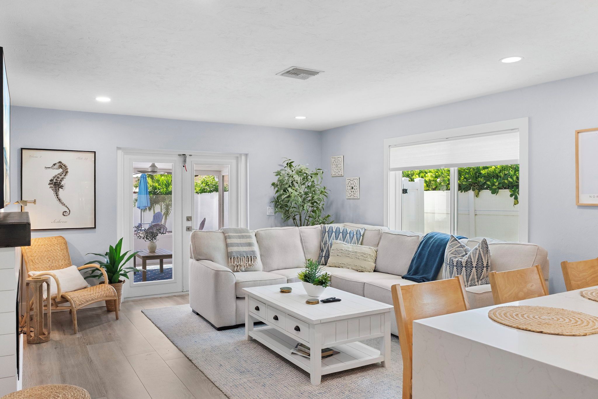 A modern living room with a sofa, coffee table, and chairs. There is a door leading to an outdoor area with plants.