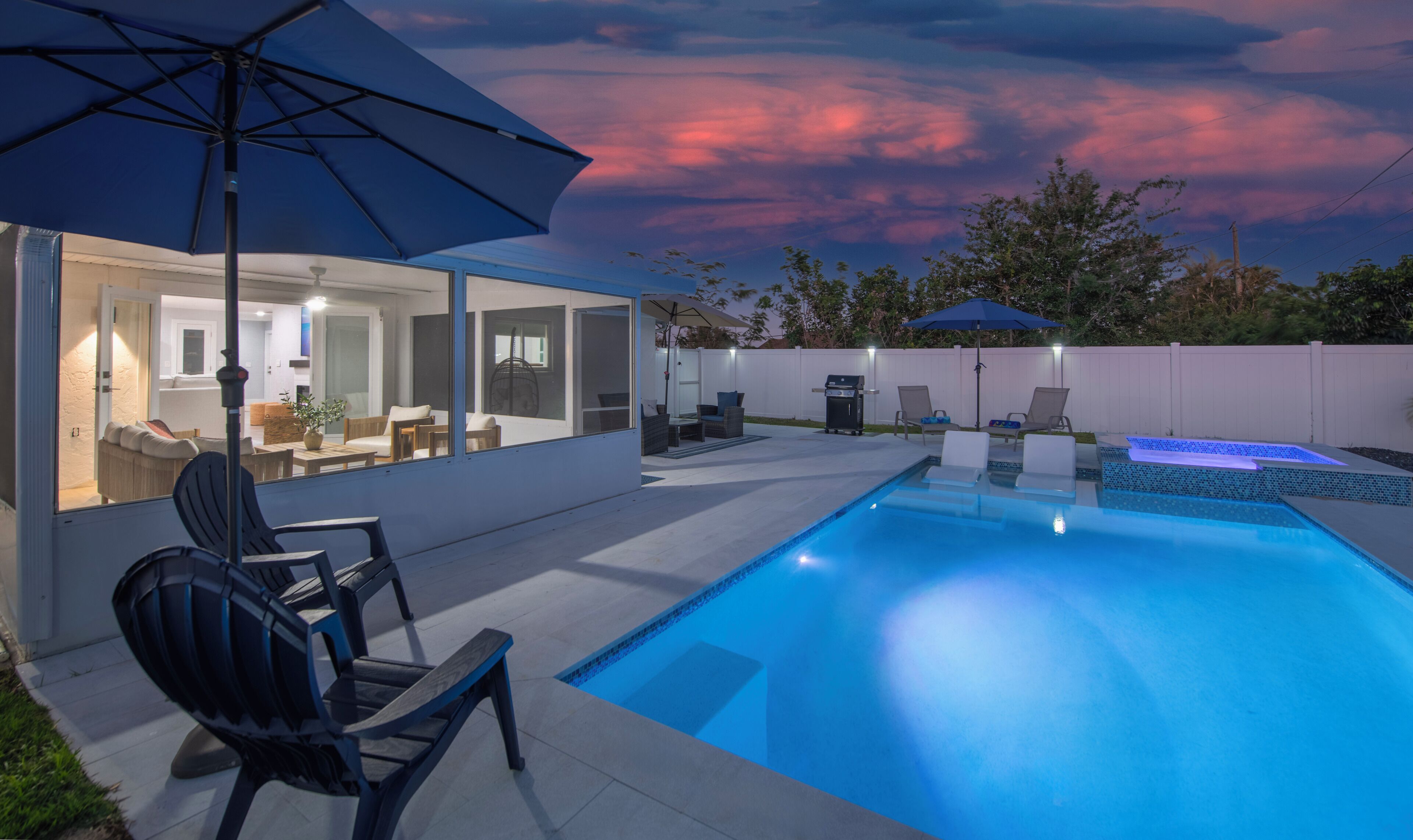 A modern outdoor pool area with a glass-enclosed patio, lounge chairs, and a barbecue grill.