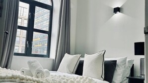 A modern hotel room with a large window, a bed with white bedding, and a black nightstand.