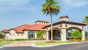 A two-story building with a red-tiled roof, a central entrance with a clock, and a palm tree in the foreground.