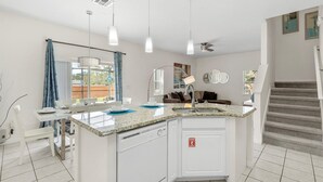 A modern kitchen with a central island, pendant lights, and a view to the outside.