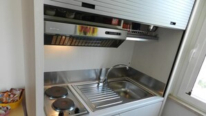 Pieni, käytännöllinen keittokomero, jossa on ruostumattomasta teräksestä valmistettu pesuallas, kaksi liesilevyä ja pieni ikkuna.