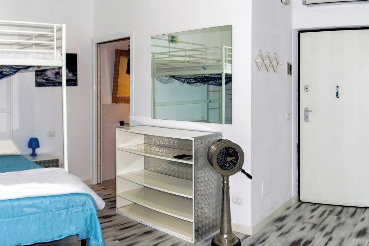 Un lit superposé avec une couverture bleue, un miroir au-dessus et une petite étagère avec un ventilateur.