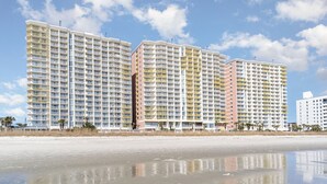 Un hotel frente a la playa con varios edificios altos, una playa de arena y un cielo despejado.