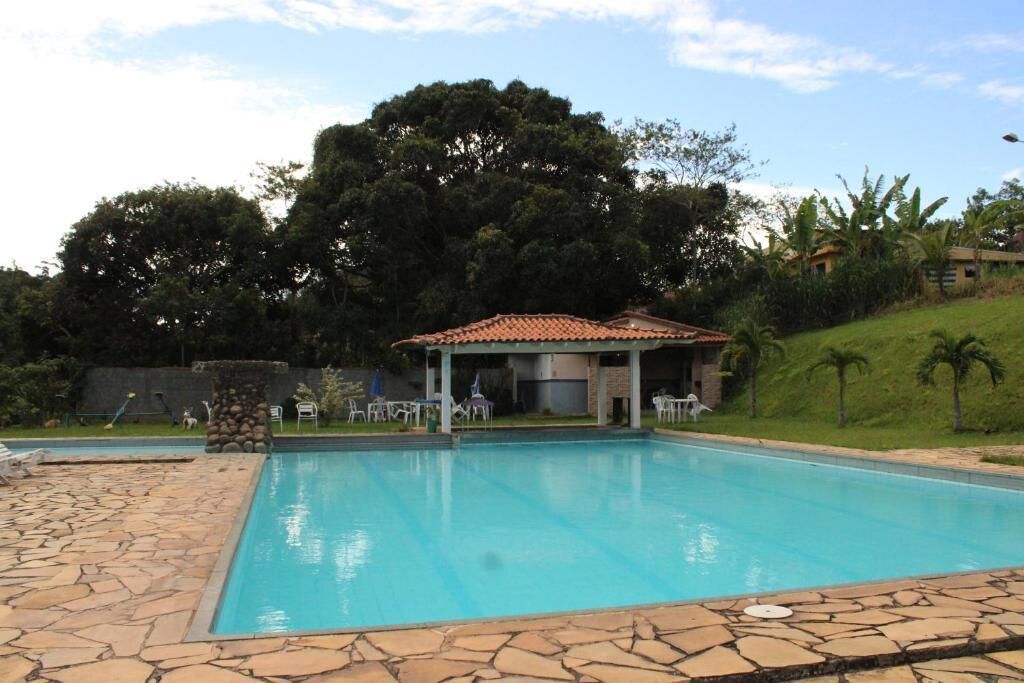 Una piscina con terraza de piedra, un área de estar cubierta y exuberante vegetación de fondo.