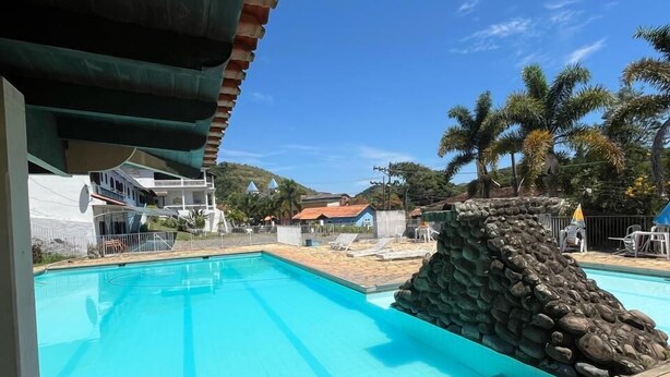 Una piscina con un muro de piedra y vistas a casas y palmeras al fondo.