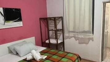 Quarto de hotel com cama, janela com cortinas, mesa de cabeceira e televisão fixada na parede.