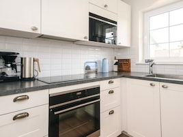 Uma cozinha moderna com armários brancos, forno embutido, micro-ondas e cafeteira.