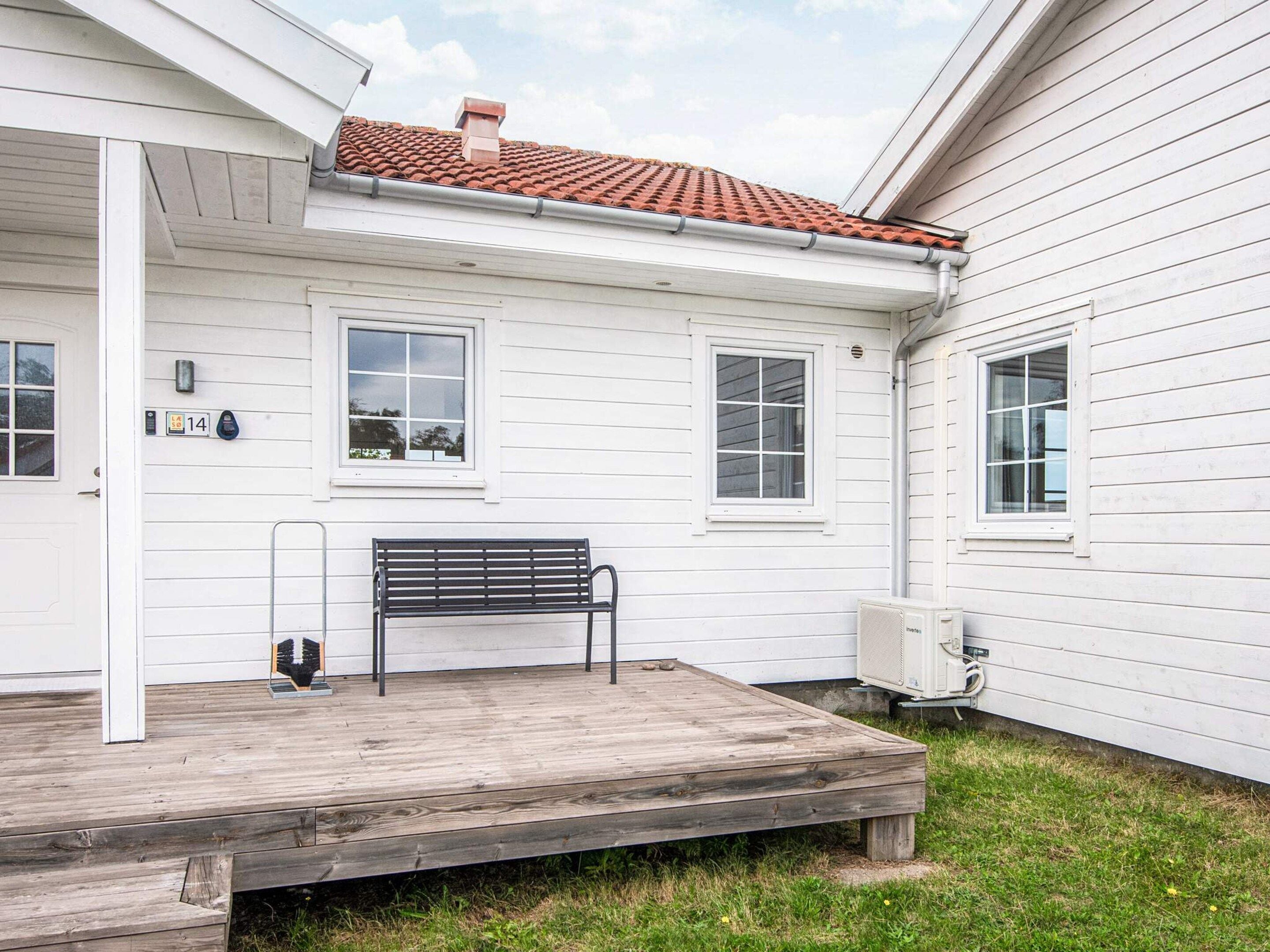 A white building with a tiled roof, a wooden deck, and a bench.