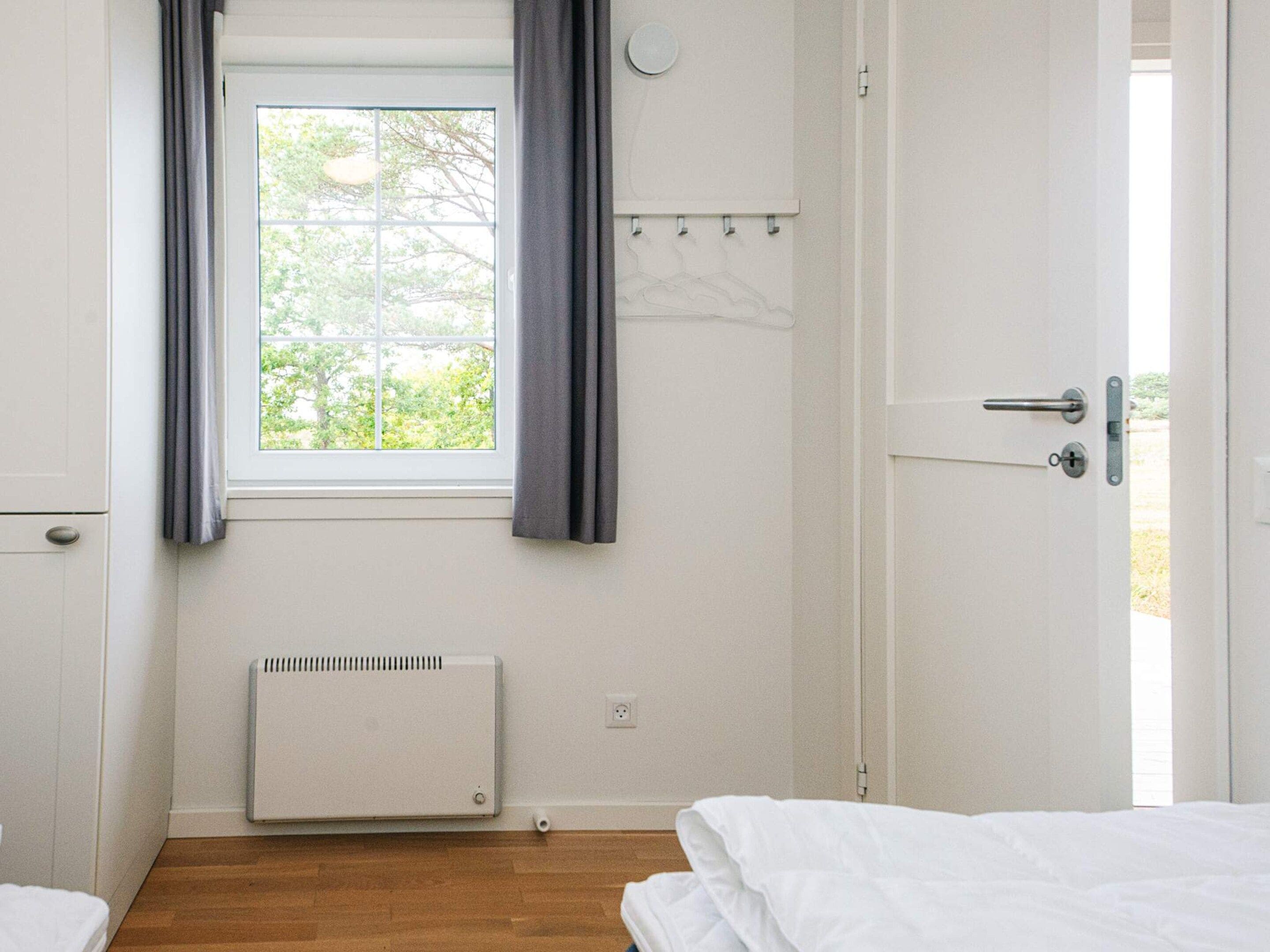 A room with a window, a radiator, a door, and a bed.
