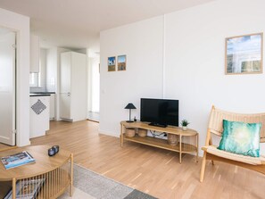 Una sala de estar moderna con un televisor, una silla de mimbre y una mesita con revistas.