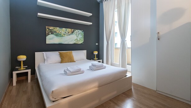 Une chambre à coucher moderne avec un grand lit, du linge de lit blanc, un tableau au mur et deux lampes de chevet.