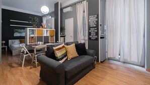 Un salon moderne avec un canapé gris, un plancher en bois et un coin repas comprenant une table et des chaises blanches.