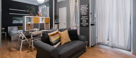A modern living room with a grey sofa, wooden flooring, and a dining area with a white table and chairs.