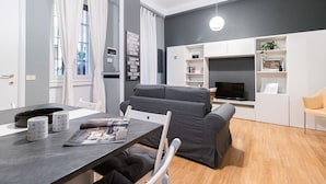Un salon moderne avec un canapé gris, une table à manger sur laquelle reposent deux tasses, un magazine et un téléviseur fixé à un mur blanc.