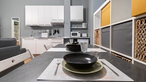 Une cuisine moderne avec des meubles blancs, un four à micro-ondes et une table à manger agrémentée d’un saladier, d’une assiette et de couverts.