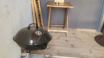 A portable grill with wheels, a wooden chair, and a small table with a sign in a corner.