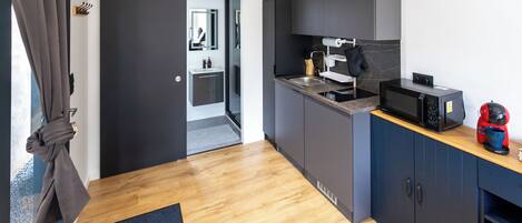 Una cocina compacta con microondas, cafetera y un lavamanos pequeño.