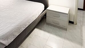 A neatly made bed with a white bedspread, a grey headboard, and a bedside table with drawers.