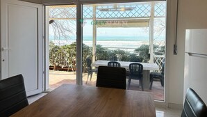 A dining area with a table and chairs, a refrigerator, and a view of the ocean through large glass doors.
