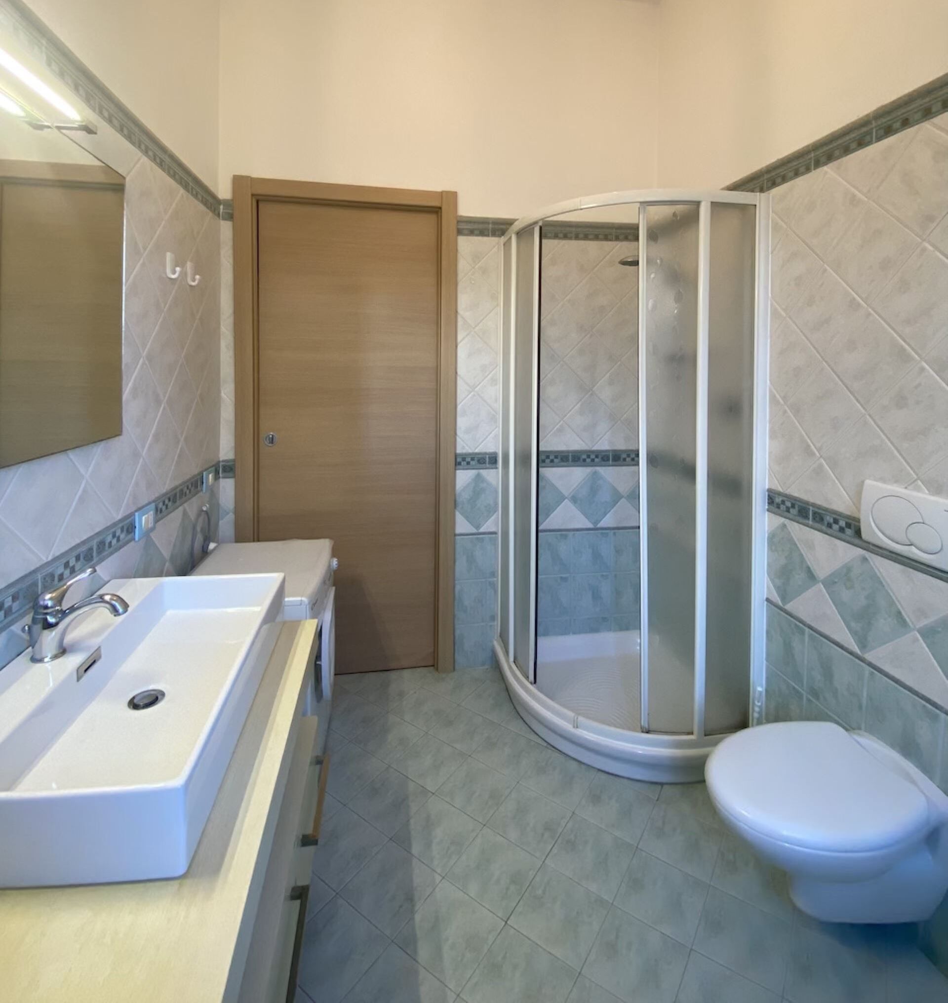 A bathroom with a sink, mirror, toilet, and shower enclosure.
