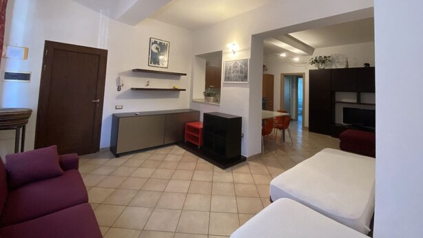 A living room with a sofa, a small table, and a kitchen area with a counter and shelves.