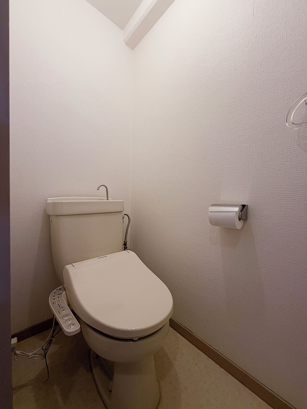 A small, plain bathroom with a white toilet, a toilet paper holder, and a visible electrical outlet.