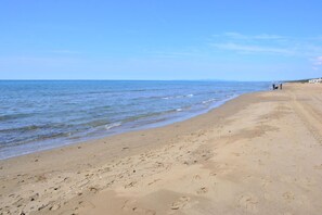 Ein weiter Sandstrand mit sanften Wellen, blauem Himmel und ein paar Personen in der Ferne.