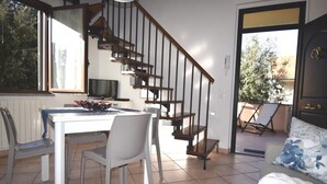 Een eethoek met een tafel en stoelen, een trap en een bank met een decoratief kussen.