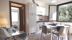 Een moderne keuken met witte kasten, een eettafel en stoelen. Er is een raam met uitzicht op bomen.