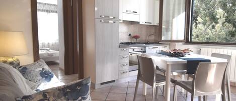 Una cocina moderna con armarios blancos, una mesa de comedor y sillas. Se ve una ventana con vistas a árboles.