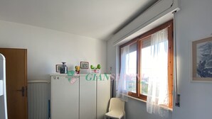 A bedroom with a bed, a chair, a wardrobe, and a window with curtains. - THREE-ROOM APARTMENT SLEEPS 5 IN THE CONCHIGLIA (San Vincenzo)