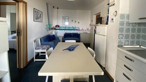 A compact living space with a dining table, two sofas, a kitchen area, and a small refrigerator. - THREE-ROOM APARTMENT SLEEPS 5 IN THE CONCHIGLIA (San Vincenzo)