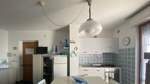 A compact kitchen with a dining area, white cabinets, a stove, and a clock on the wall. - THREE-ROOM APARTMENT SLEEPS 5 IN THE CONCHIGLIA (San Vincenzo)