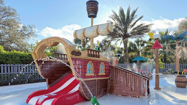 Un espace de jeux sur le thème des pirates, avec un toboggan, une cabane en forme de bateau et une figurine de crocodile.