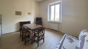 A room with a wooden dining table, chairs, a ceiling fan, a window with a view, and a radiator.