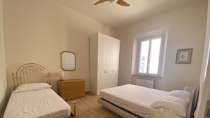 A bedroom with two beds, a dresser, a wardrobe, a window, and a ceiling fan.