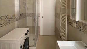 A compact bathroom with a glass-enclosed shower, a washing machine, and a large sink.