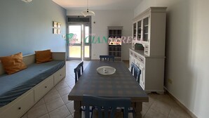 A dining area with a table and chairs, a sofa with cushions, a cabinet, and a ceiling fan. - TWO-ROOM APARTMENT SLEEPS 4 IN THE LA PIANA AREA (San Vincenzo)
