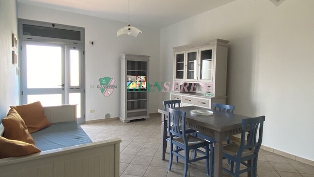 A dining area with a table and chairs, a white cabinet with glass doors, and a ceiling light fixture. - TWO-ROOM APARTMENT SLEEPS 4 IN THE LA PIANA AREA (San Vincenzo)