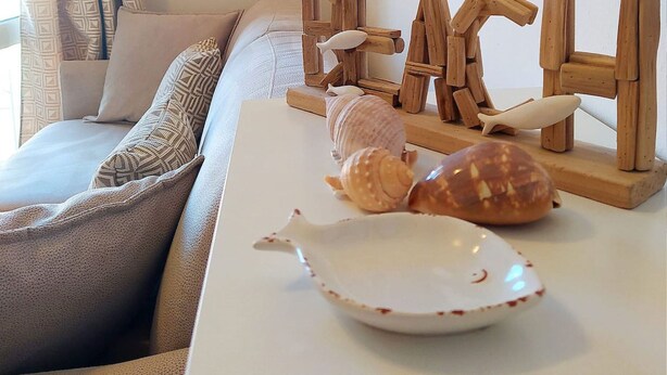 A cozy living room with a sofa, decorative wooden letters spelling "FISH," seashells, and a white plate on a white table.