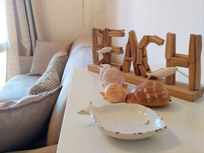 A cozy living room with a sofa, decorative wooden letters spelling "FISH," seashells, and a white plate on a white table. - THREE-ROOM APARTMENT, SLEEPS 4, SHELL AREA (San Vincenzo)