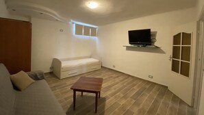 A small, well-lit room with a bed, a small table, a TV mounted on the wall, and a window with blinds. - 5 beds with garden and air conditioning (San Vincenzo)